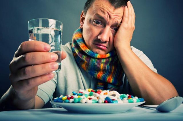 Een man met een glas in zijn hand kijkt naar een bord met pillen
